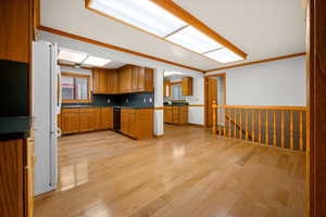 Kitchen featuring wood finish cabinetry, dark countertops, crown molding, light wood-style flooring, and freestanding refrigerator