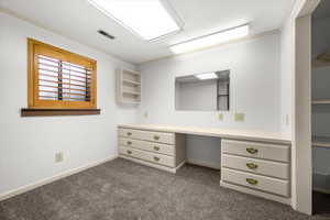 Walk in closet with built in study area and dark carpet