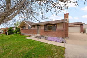 Ranch-style home featuring brick siding, a front yard, a chimney, and concrete driveway