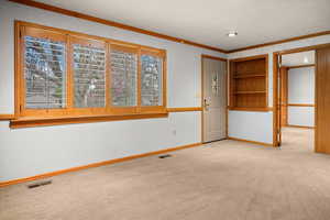 Unfurnished room featuring light colored carpet, crown molding, and built in shelves