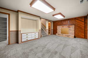Unfurnished living room featuring ornamental molding, light colored carpet, and wood walls