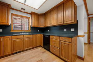 Kitchen with dark countertops, wood finish cabinetry, crown molding, light wood-style flooring, and dishwasher