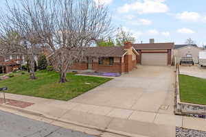 Ranch-style home with brick siding, driveway, a front lawn, and a chimney