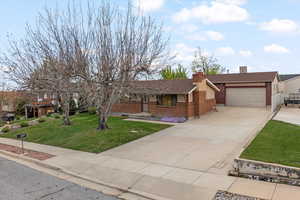 Ranch-style home featuring driveway, brick siding, a front yard, an attached garage, and a chimney
