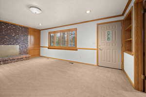 Unfurnished living room with light colored carpet, crown molding, a textured ceiling, and a brick fireplace