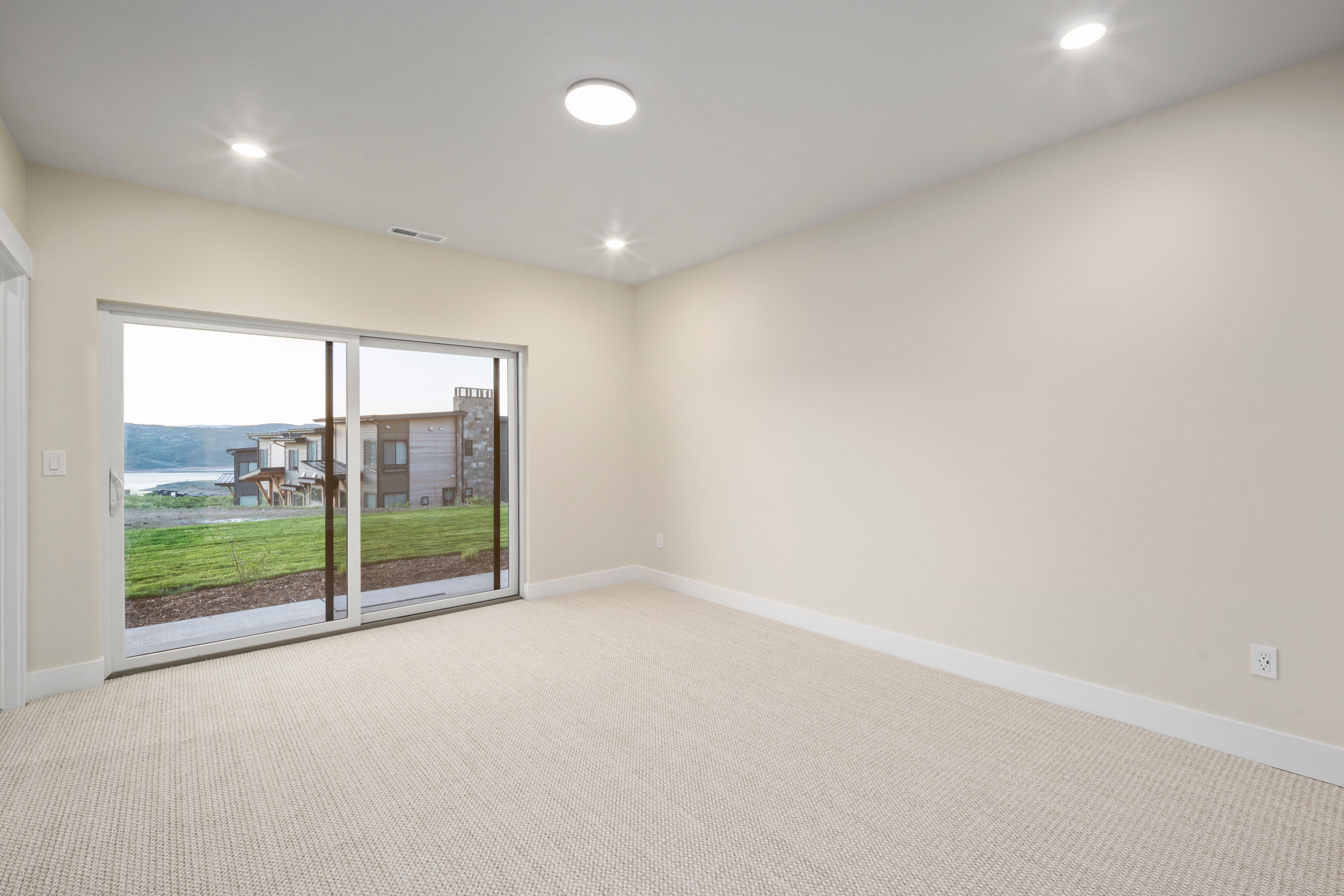Bright room featuring light-colored walls, recessed ceiling lighting, textured carpet flooring, and a large sliding glass door