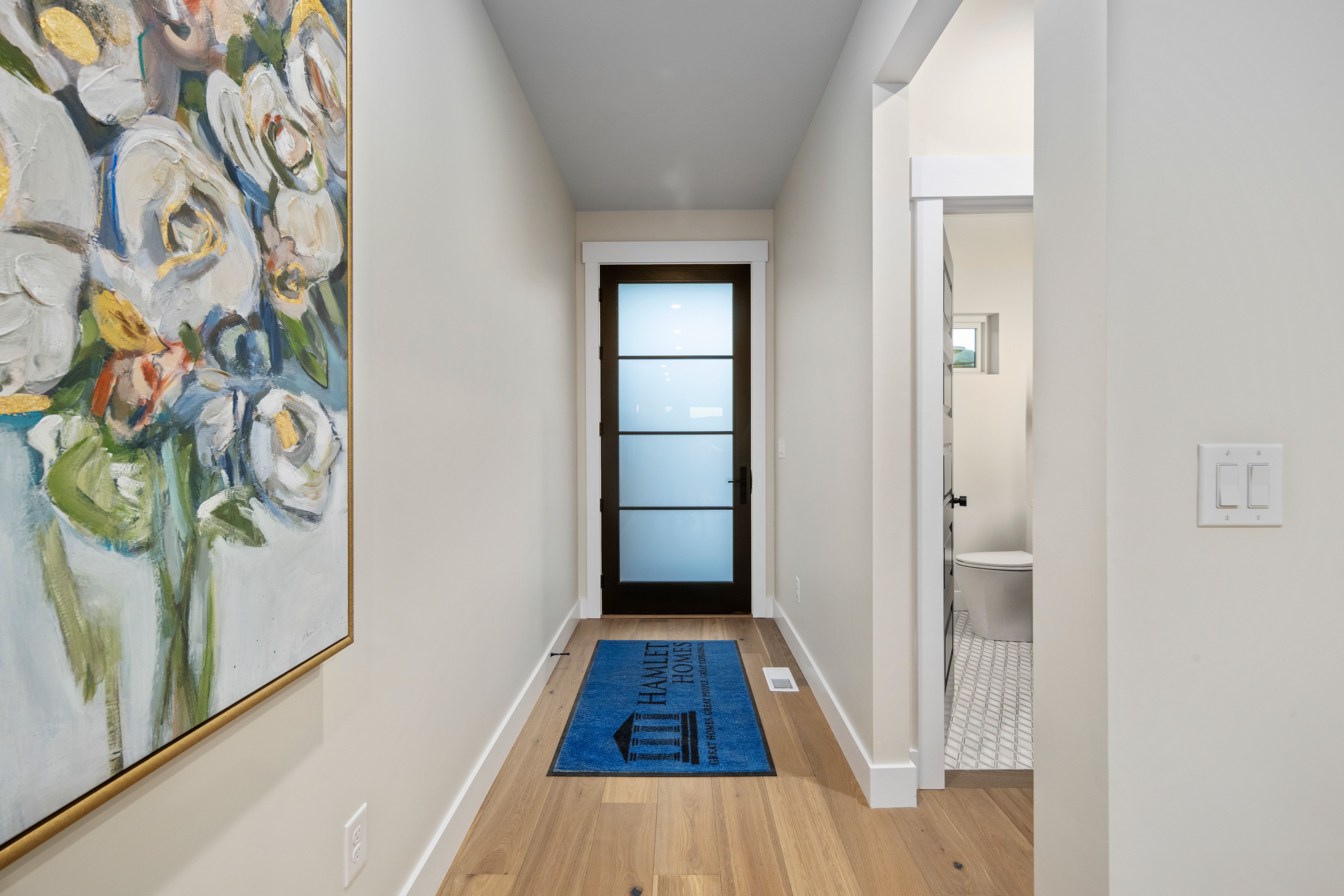 Entryway featuring wood-finish flooring, white baseboards, and a dark-framed door with frosted glass panels