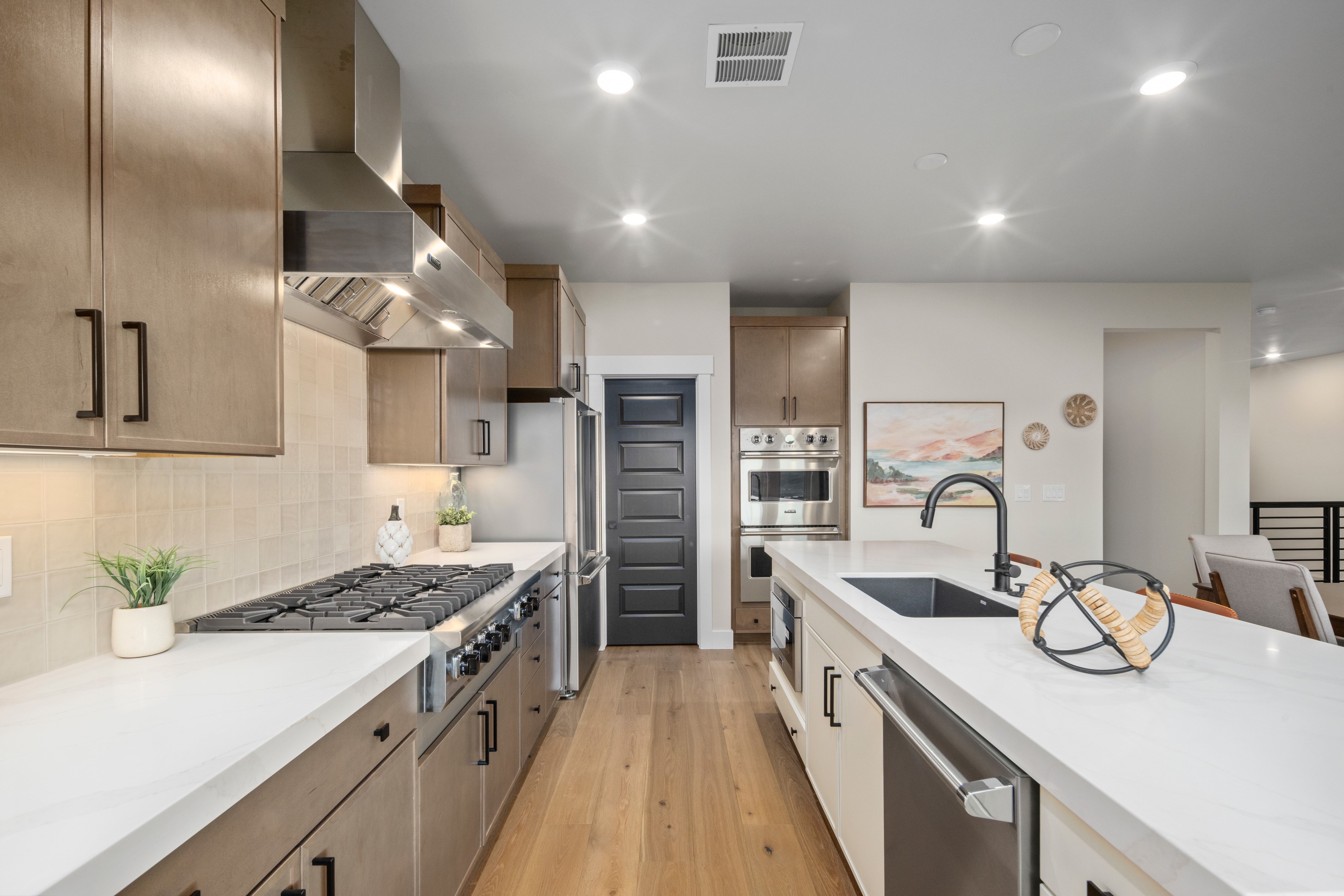 Gourmet kitchen featuring a professional-grade range, stainless steel appliances, light wood-finish cabinetry with black hardware, white countertops, and wood-finish flooring