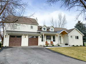 View of front of property with board and batten siding, driveway, a chimney, an attached garage, and a porch