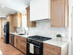 Kitchen featuring black appliances, backsplash, quartzite countertops, and wood flooring