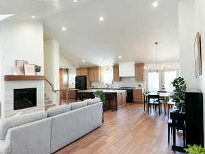 Living room with wood flooring, a high end fireplace, and vaulted ceiling