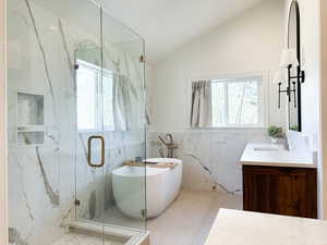 Full bathroom featuring 2 vanities, a freestanding tub, lofted ceiling, and tile walls