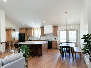 Kitchen and Dining featuring a chandelier, a center island, black appliances, wood flooring, custom cabinetry, and quartzite countertops