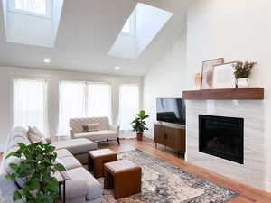 Living room with light wood-style floors, healthy amount of natural light, a high end fireplace, and vaulted ceiling