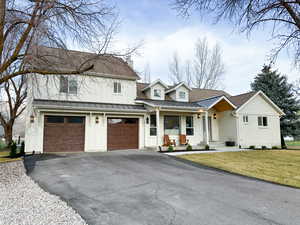 Modern inspired farmhouse with covered porch, board and batten siding, driveway, a standing seam roof, and an attached garage