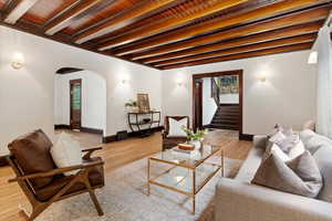 Living room featuring arched walkways, light wood finished floors, and beamed ceiling