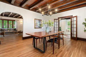 Dining area featuring french doors, a wooden ceiling with exposed beams, arched walkways, and light wood finished floors