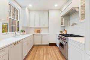 Kitchen featuring stainless steel stove, white cabinets, light wood-style flooring, light stone counters, and recessed lighting