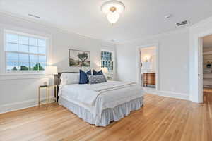 Bedroom with ornamental molding, light wood-style flooring, and connected bathroom
