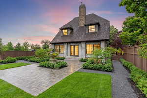 Back of property at dusk featuring french doors, a fenced backyard, a shingled roof, and a chimney
