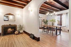 Hallway featuring arched walkways, hanging lights, light wood-type flooring, and a wooden ceiling with exposed beams