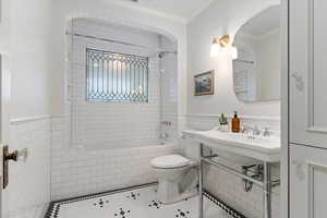 Full bath featuring tile walls, tile patterned floors, ornamental molding, tiled shower / bath, and a wainscoted wall