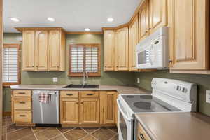 Kitchen featuring white appliances, light wood finish cabinets, light countertops, recessed lighting, and dark tile patterned flooring