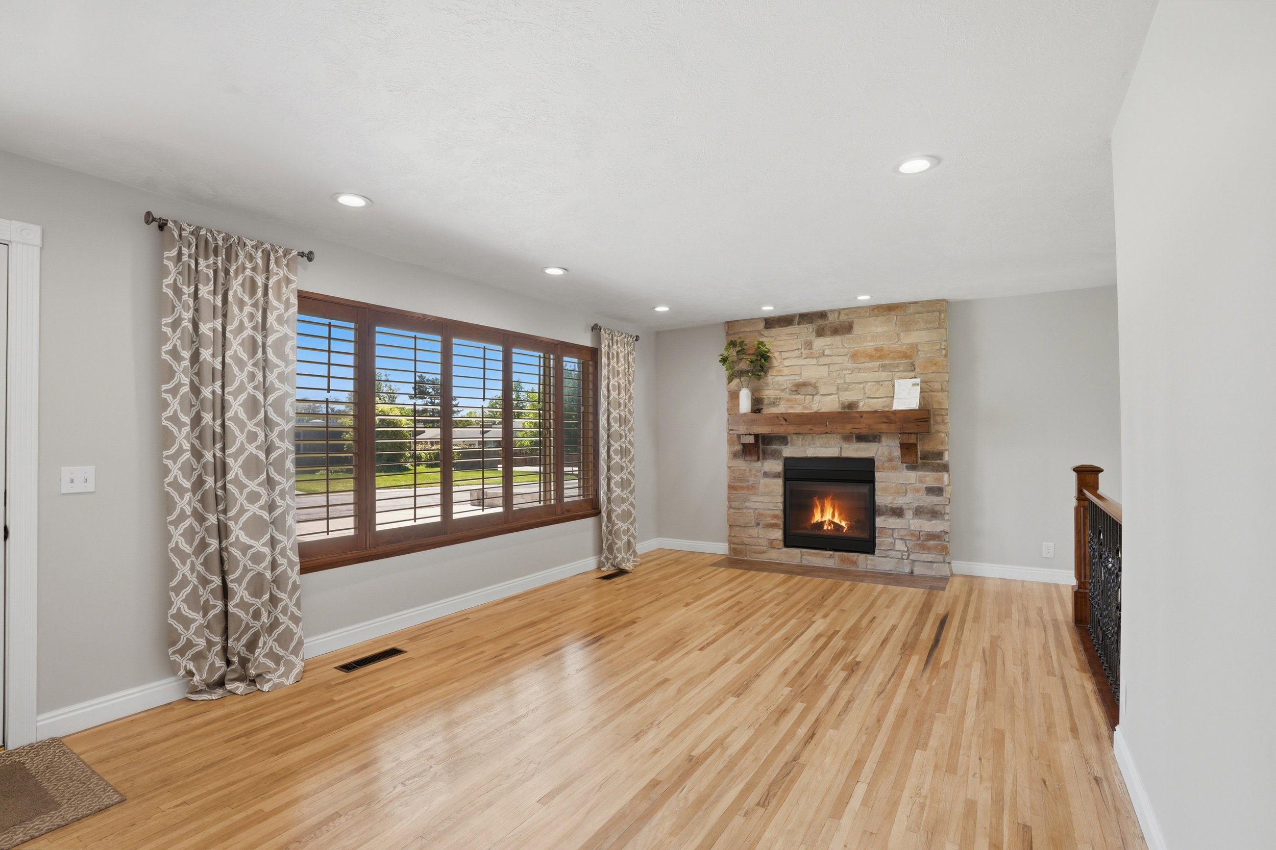 Hardwood flooring throughout featuring a stone-clad fireplace with a rustic wood mantel