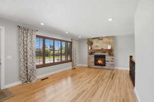Hardwood flooring throughout featuring a stone-clad fireplace with a rustic wood mantel
