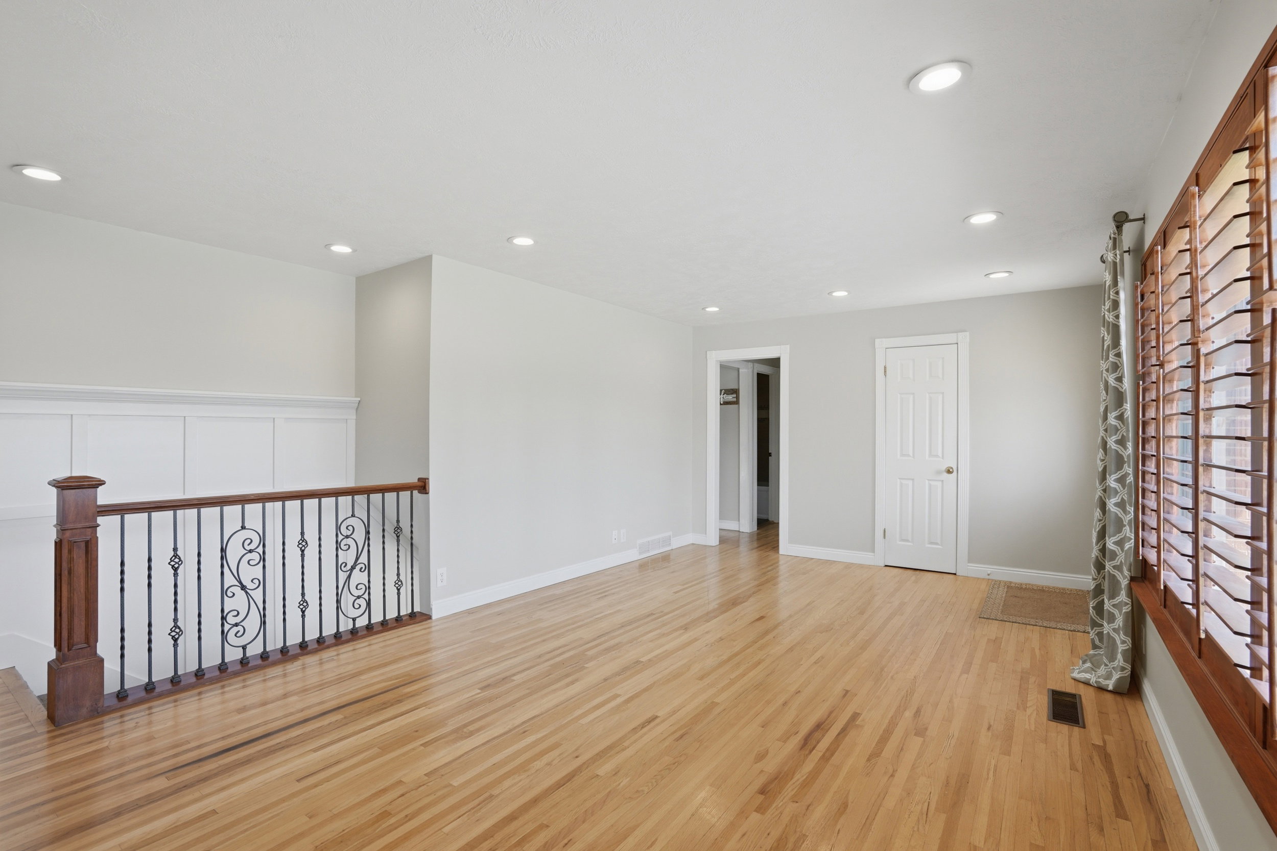 Spacious interior featuring wood-finish flooring, recessed lighting, and a decorative wrought iron railing with a wood-stained top rail and newel post