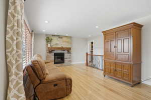 Living room featuring light wood-style flooring, a stone fireplace, and recessed lighting