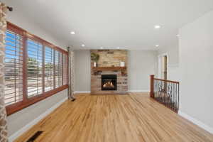 Living area featuring wood-finish flooring, a stone-clad fireplace with a wood mantel, and expansive windows with plantation shutters