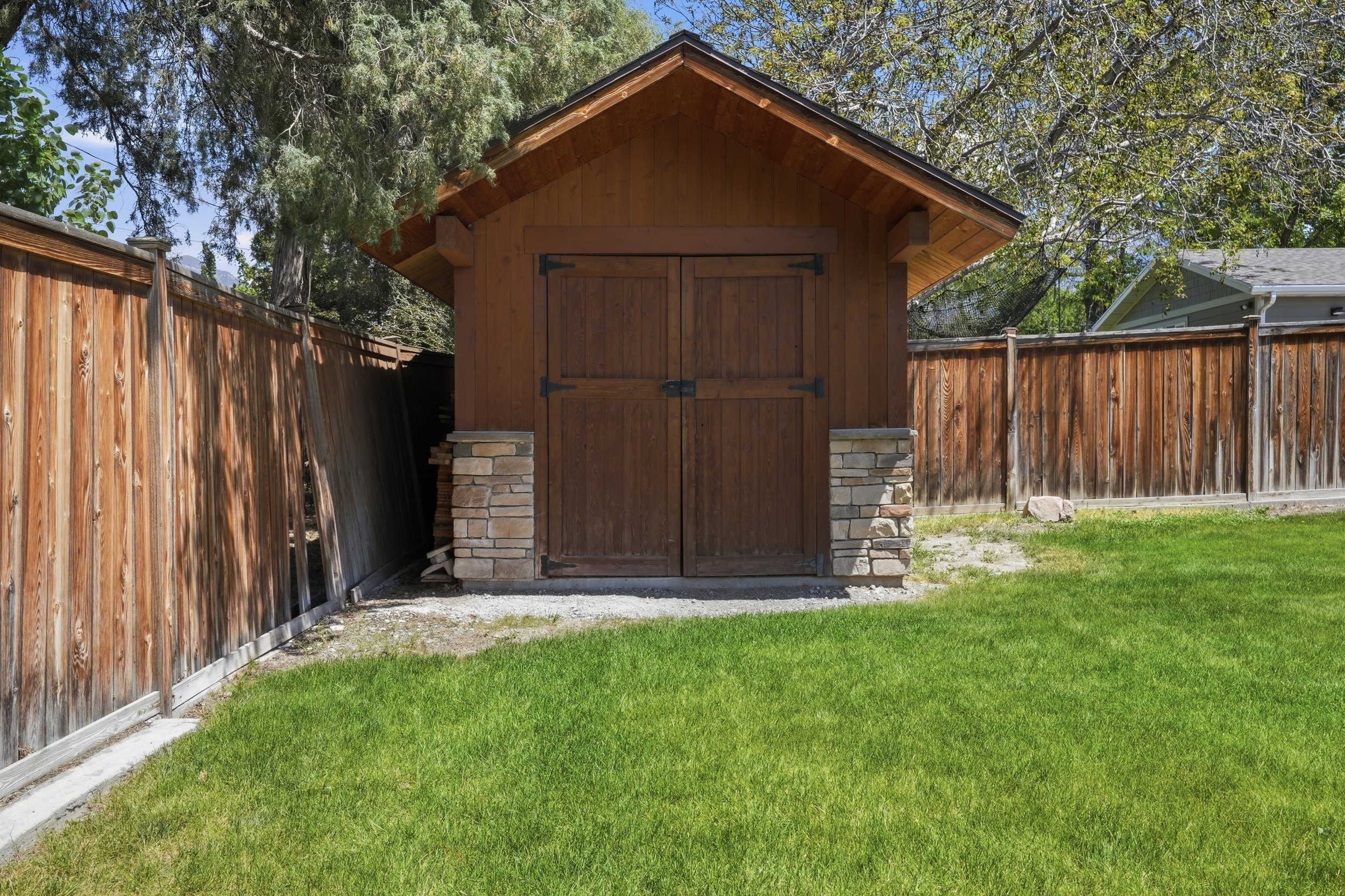 Wood-sided storage shed featuring stone veneer accents, double doors, and an overhanging roofline