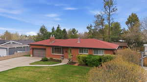 Rambler-style home with concrete driveway, brick siding, a garage, and a chimney