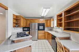 Kitchen with open shelves, black appliances, wood finish cabinetry, light tile patterned flooring, and a peninsula