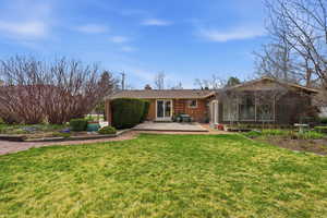 Rear view of property featuring a chimney, brick siding, a patio, and a yard