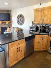 Kitchen featuring dark stone counters, stainless steel appliances, a stone fireplace, stone tile floors, and tasteful backsplash