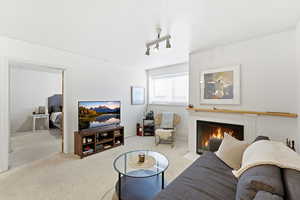 Living room with a fireplace, light colored carpet, rail lighting, and a textured ceiling