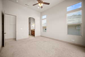 Unfurnished bedroom featuring arched walkways, light carpet, connected bathroom, a ceiling fan, and a high ceiling