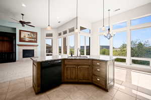Kitchen with light stone counters, black dishwasher, a tile fireplace, a kitchen island with sink, and open floor plan