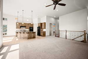 Kitchen featuring light carpet, a breakfast bar area, wood finish cabinetry, a ceiling fan, and a large island with sink