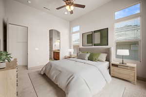 Bedroom with light carpet, arched walkways, connected bathroom, and a ceiling fan