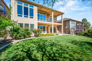 Back of property with a balcony, stucco siding, and a lawn