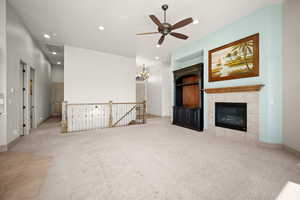 Unfurnished living room with light colored carpet, a ceiling fan, hanging lights, and a tiled fireplace