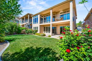 Rear view of property featuring stucco siding, a lawn, a balcony, and a patio