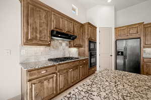 Kitchen featuring light stone counters, black appliances, and a high ceiling