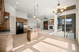 Kitchen with suspended lighting, a glass covered fireplace, light stone counters, a ceiling fan, and a breakfast bar area