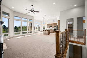 Unfurnished living room featuring a ceiling fan, light carpet, recessed lighting, and a high ceiling