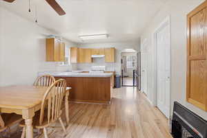 Kitchen featuring arched walkways, a peninsula, light countertops, light wood finished floors, and a ceiling fan