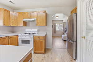 Kitchen with white range with gas cooktop, light countertops, freestanding refrigerator, and light wood finished floors